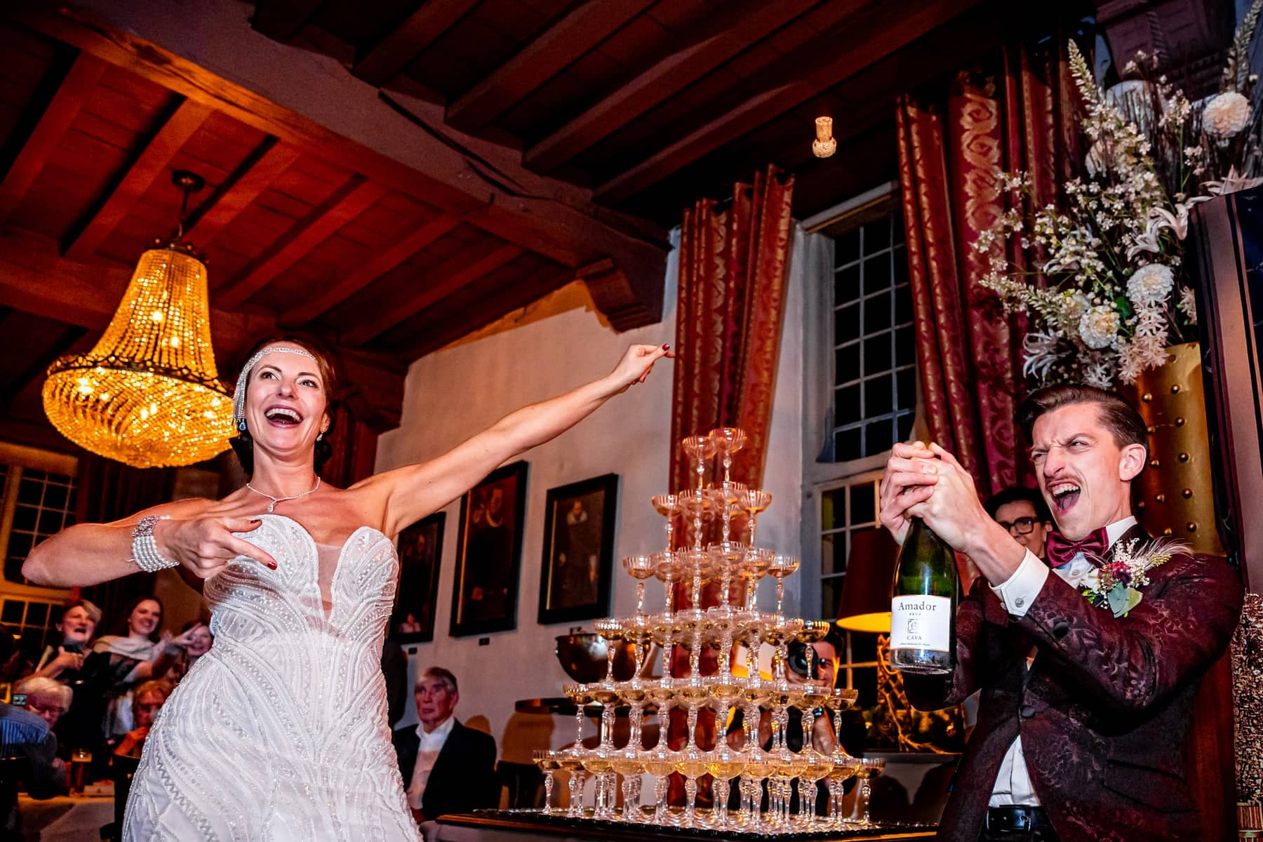 The bride cheers at a champagne tower as the groom opens the bottle