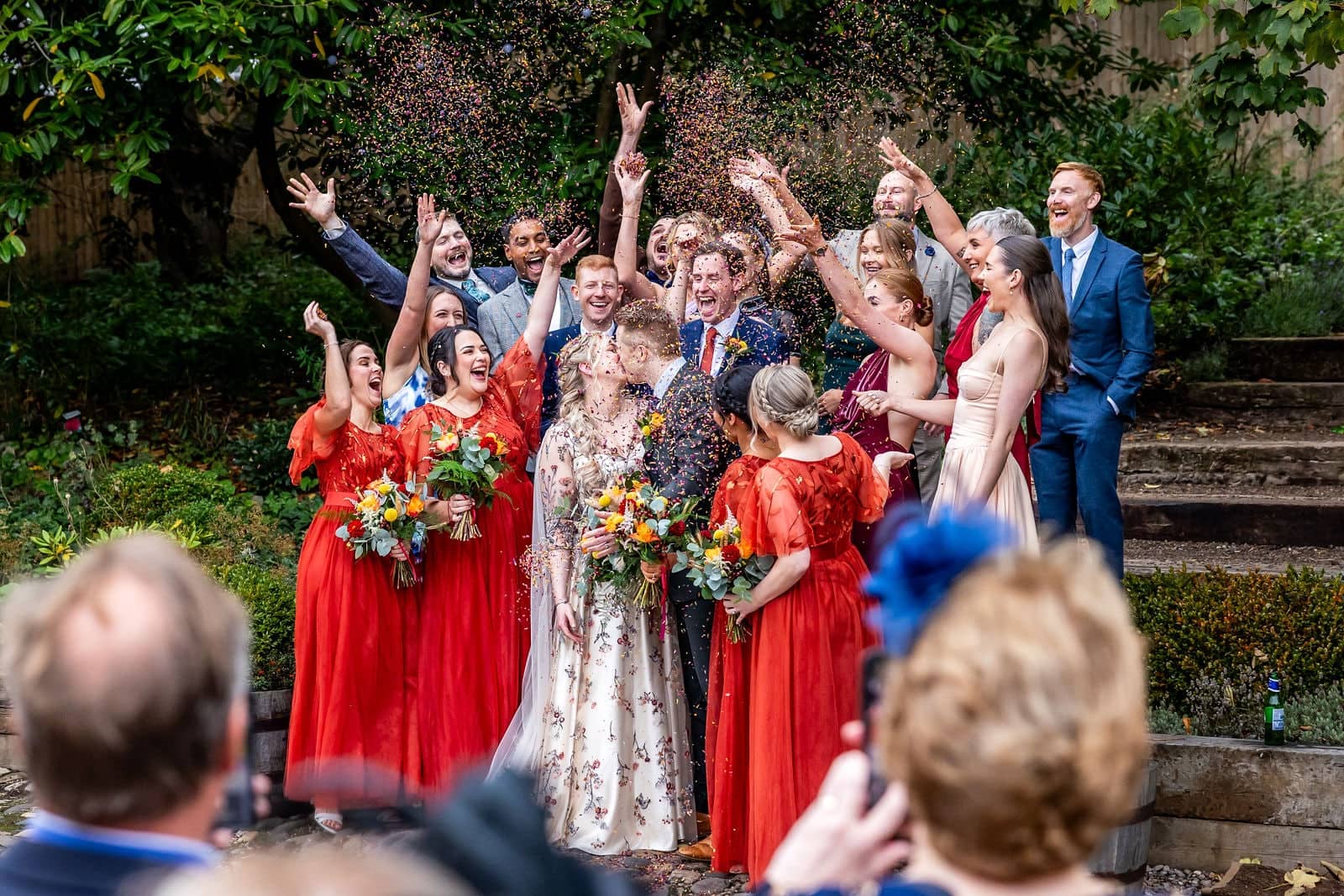 Groepsfoto met confetti: het bruidspaar, bruidsmeisjes in het rood en vrienden juichen