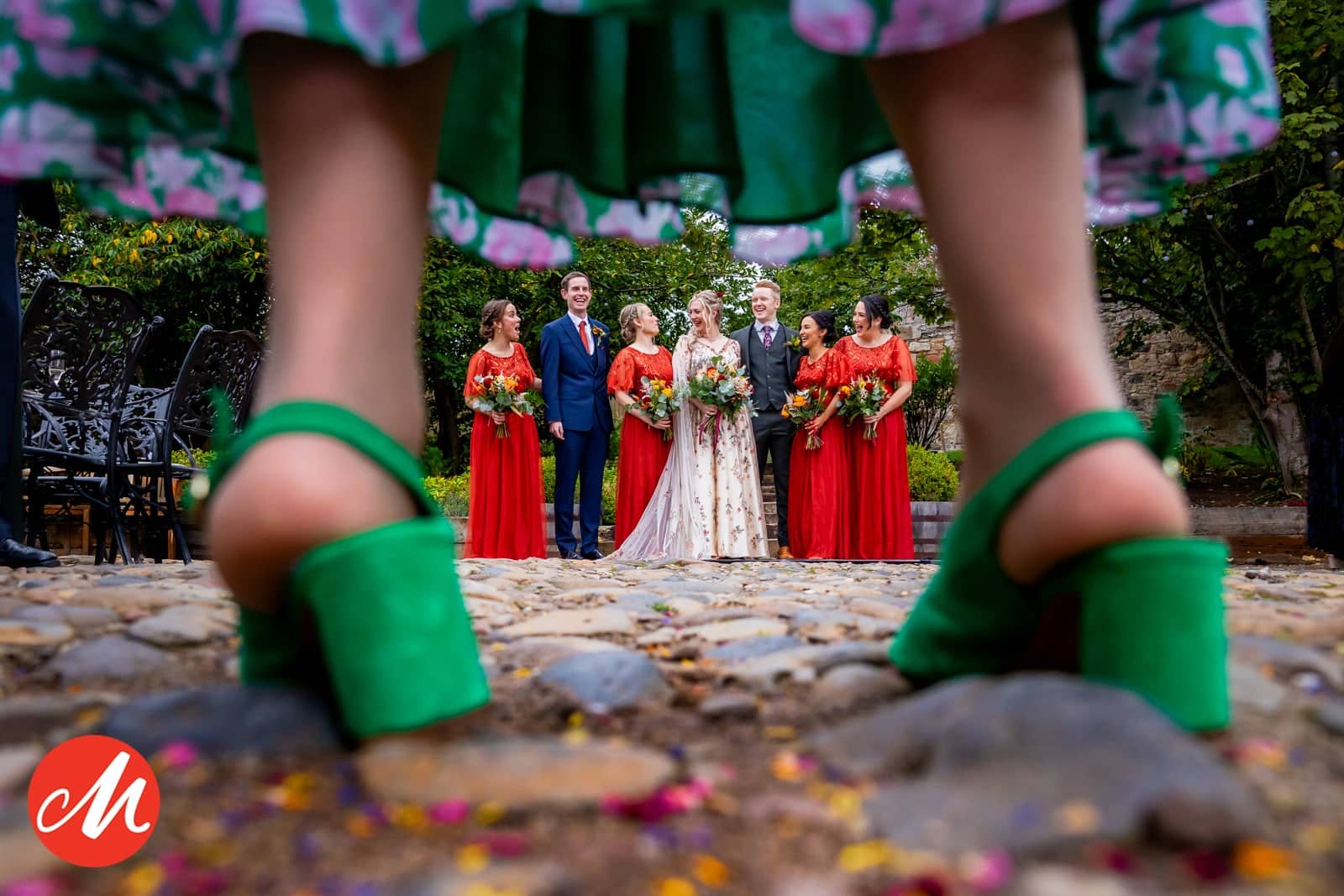 Groene hakken op de voorgrond, met het bruidspaar en bruidsmeisjes in het rood op de achtergrond