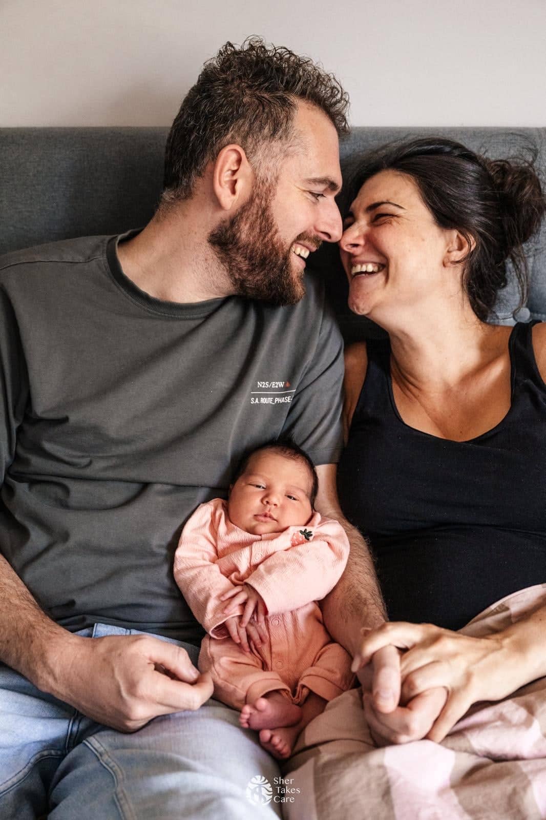 Rick and Jessica laughing at each other on the sofa, with their newborn daughter Roos between them