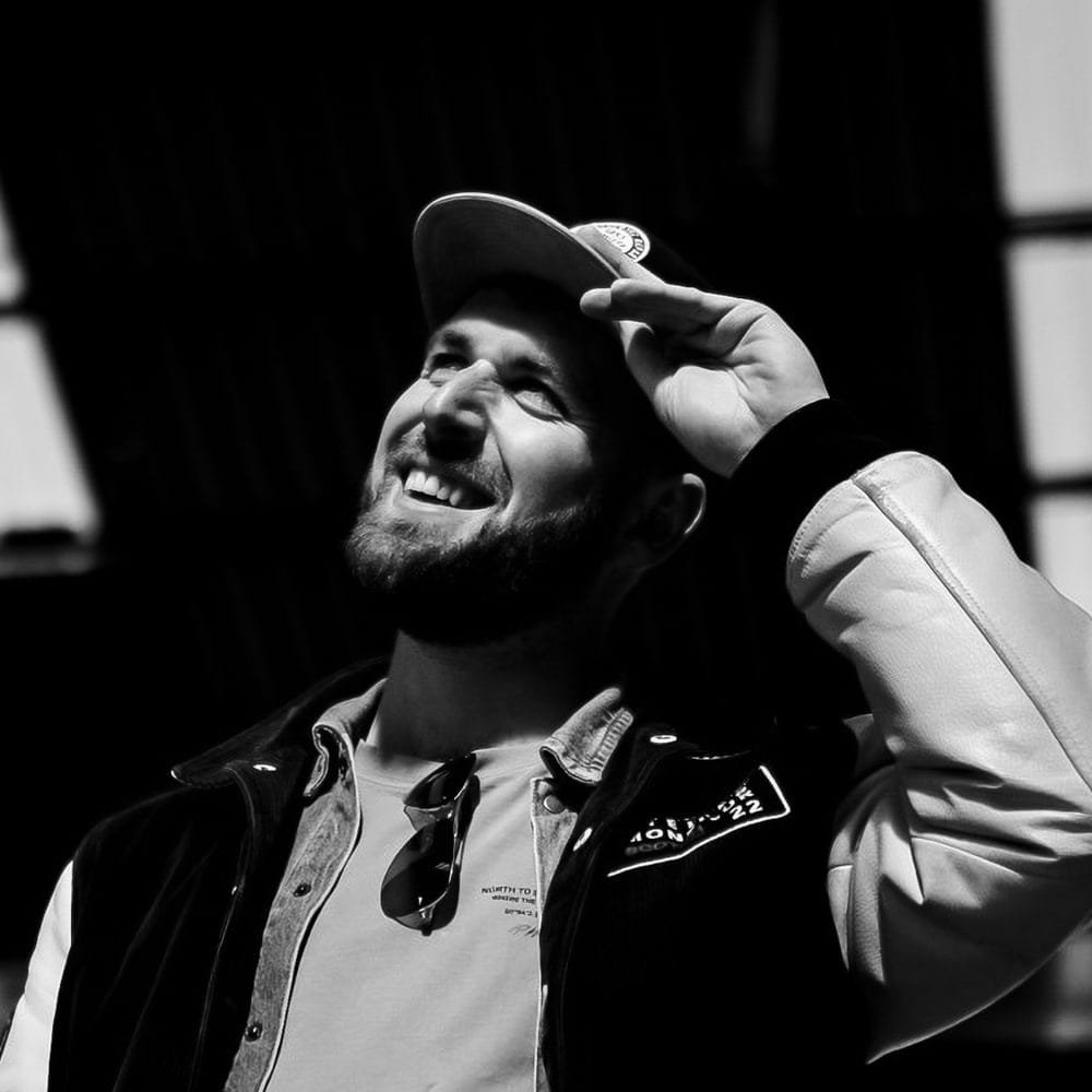 Black and white portrait of Rick de Jongh in a cap, laughing and looking up