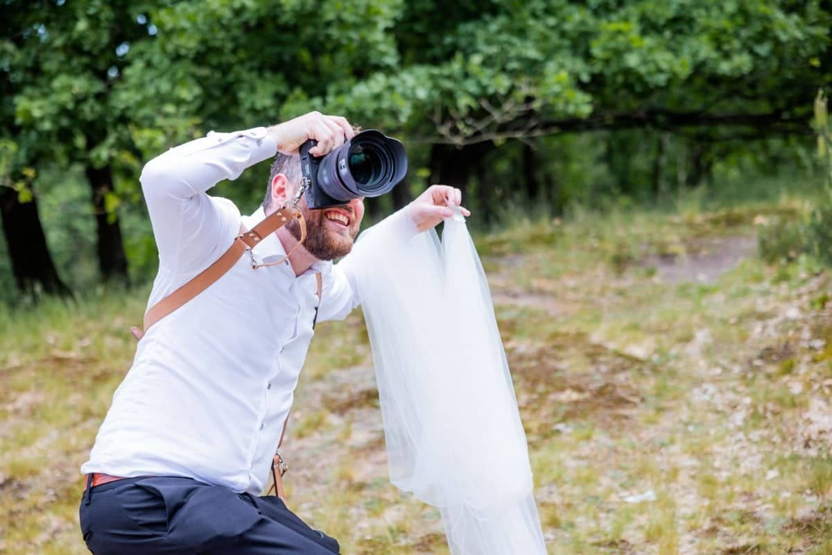 Rick de Jongh laughing as he takes a photo, holding up a veil with his other hand