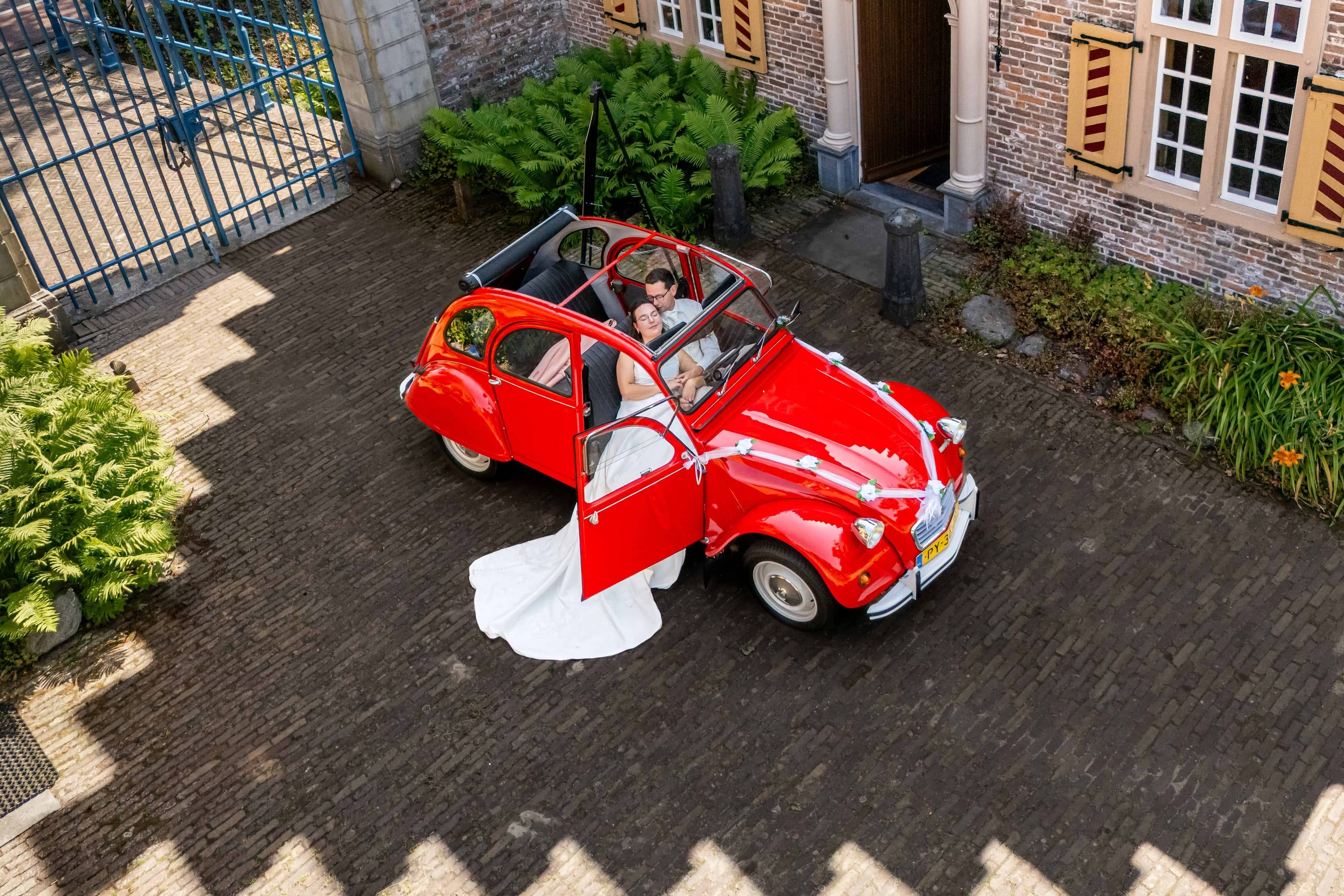 A red Citroën 2CV seen from above, the wedding dress train flowing out of the open door